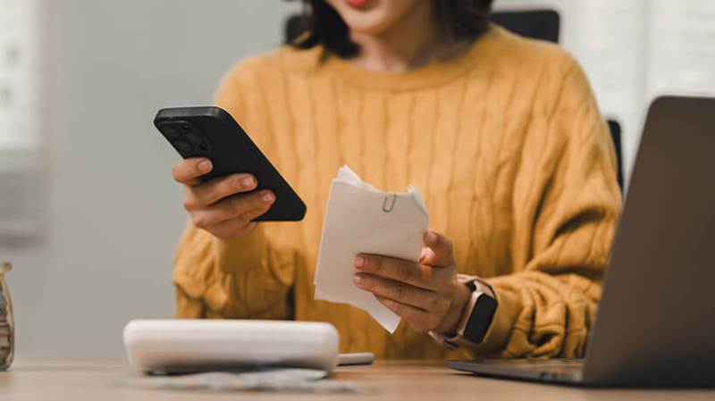 A woman scanning a paper receipt with her smartphone to track expenses in an office
